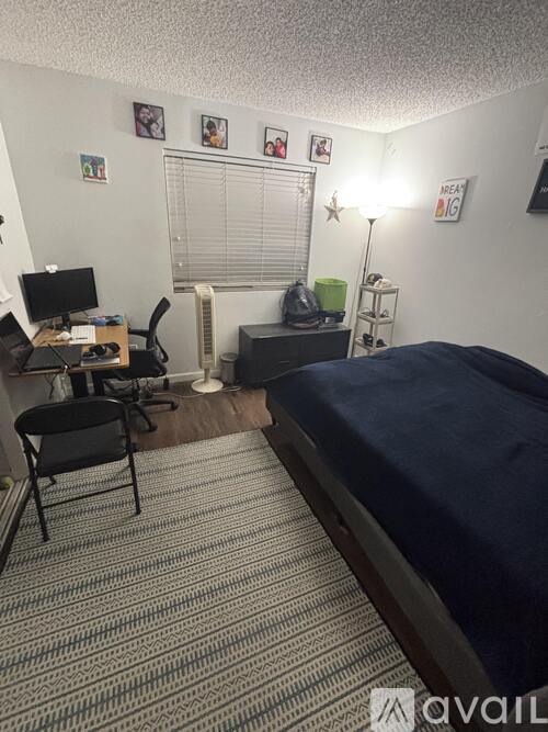 A bedroom with a bed, desk, chair, and a window with blinds.