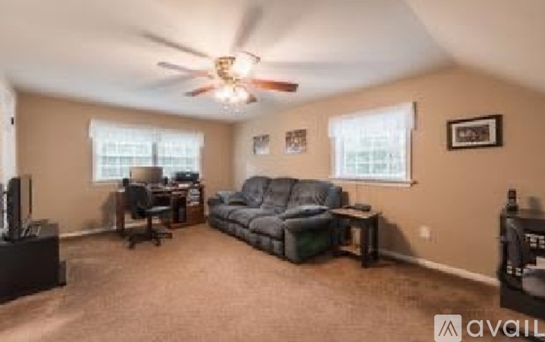 A living room with a black leather couch and a ceiling fan.