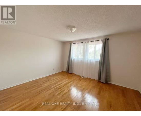 A room with wooden flooring and white walls, with a window covered by grey curtains.