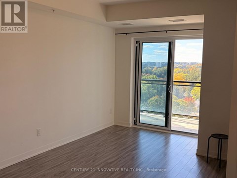 A room with a sliding glass door leading to a balcony with a view of trees and a road.