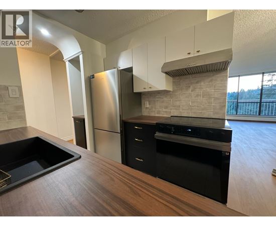 A modern kitchen with a stainless steel refrigerator and black appliances.