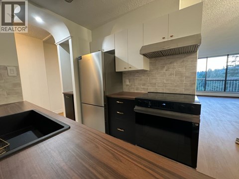 A modern kitchen with a stainless steel refrigerator and black appliances.