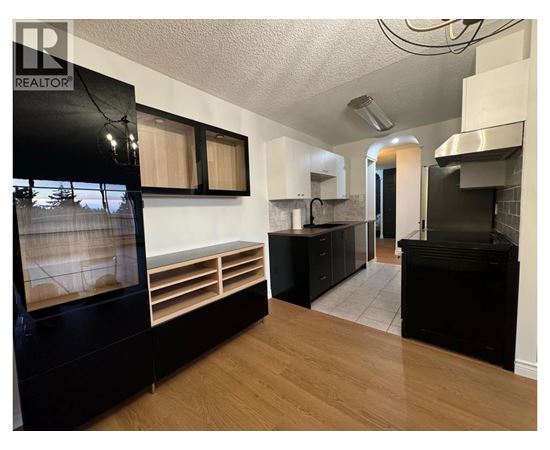 A modern kitchen with black appliances and wooden floors.