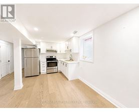 A white kitchen with wooden floors and stainless steel appliances.