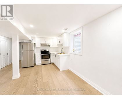 A white kitchen with wooden floors and stainless steel appliances.