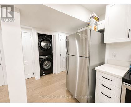 A kitchen with a stainless steel refrigerator and a washer and dryer stacked in the corner.