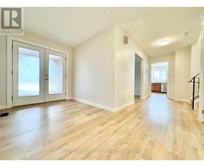 A spacious room with wooden flooring and white walls, featuring a staircase on the right side.