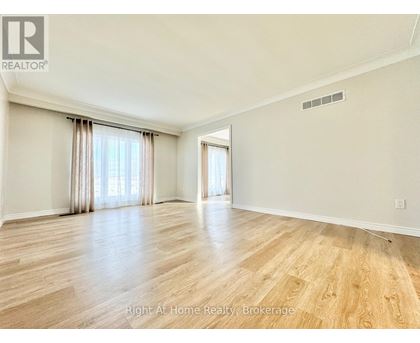 A spacious room with wooden flooring and a large window with curtains.