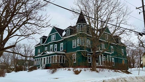 A large green house with a turret sits in the snow.