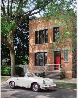 A white vintage car is parked in front of a red door.