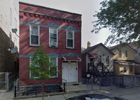 A red brick house with a white door and a tree in front.