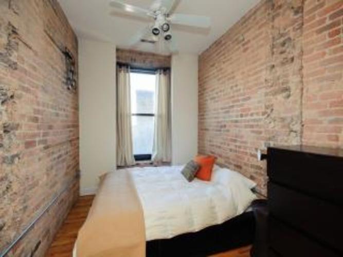 A bedroom with a brick wall and a bed with a white comforter.