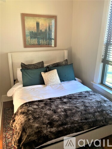 A bedroom with a white bed and a painting of a city skyline on the wall.