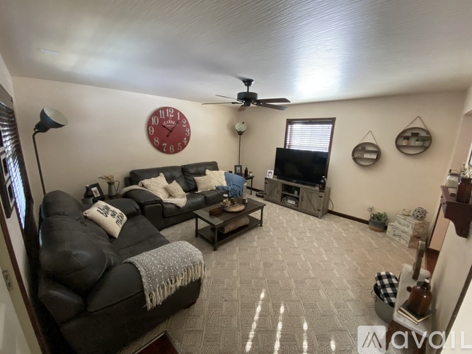 A living room with a black leather couch and a red clock on the wall.
