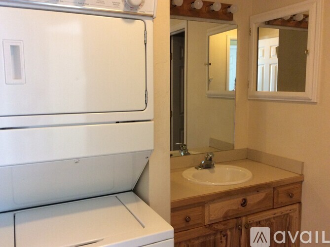 A bathroom with a white fridge, wooden vanity and a mirror.