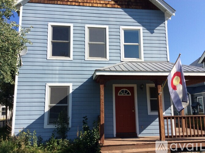 A blue house with a red door and a Colorado flag on the porch.