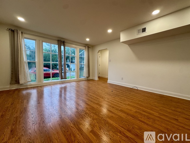 A room with wooden flooring and a large window with a view of cars and trees outside.