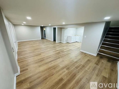A spacious room with wooden flooring and a staircase on the right side.