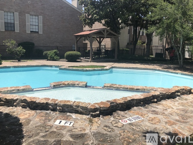 A pool surrounded by a stone wall with a gazebo in the background.