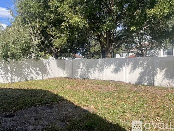 A white fence separates a grassy area from a tree-lined street.