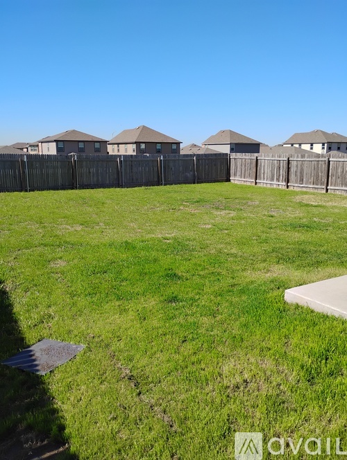 A grassy field with a fence and houses in the background.