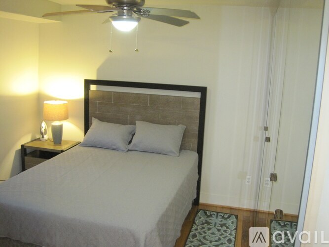 A bedroom with a bed, a ceiling fan, and a nightstand with a lamp.