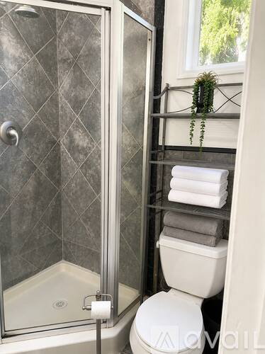 A bathroom with a toilet, a glass shower stall, and a towel rack with a plant on it.