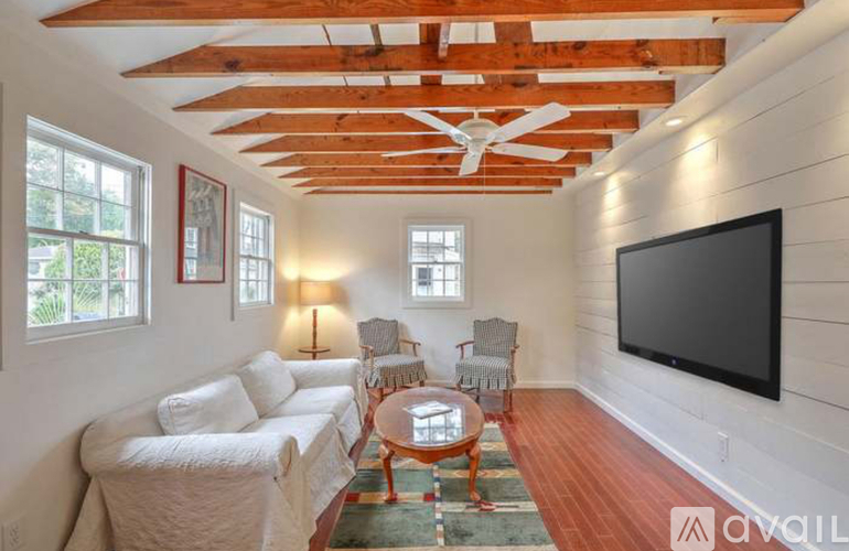 A living room with a white couch, a wooden table, and a television mounted on the wall.