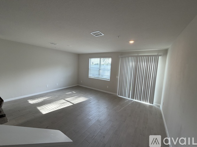 A spacious room with wooden flooring and a window with blinds.