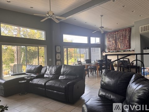 A living room with black leather furniture and a ceiling fan.