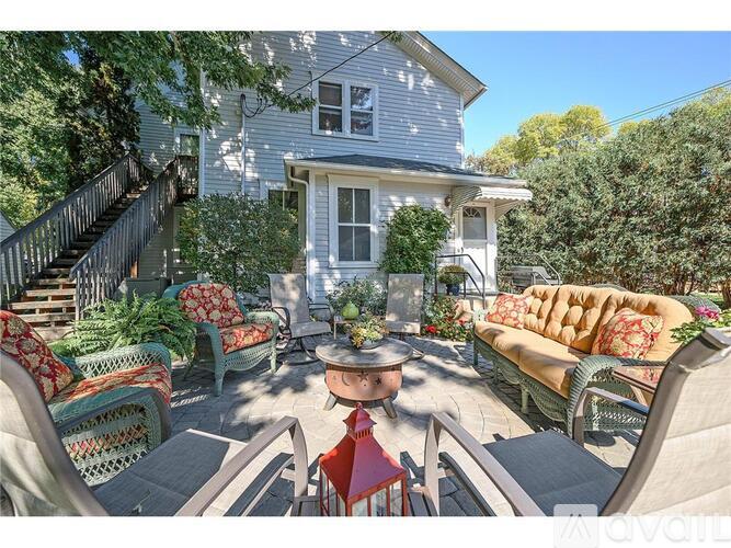 A patio with a table and chairs is surrounded by a house and trees.