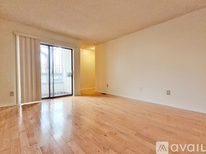 A spacious room with wooden flooring and a sliding glass door.