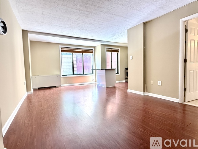 A spacious room with wooden floors and a window with blinds.