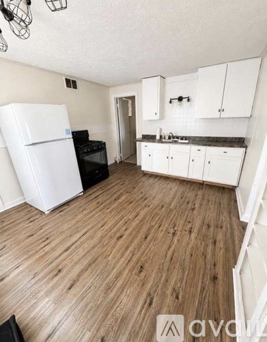 A kitchen with white appliances and cabinets with a wooden floor.