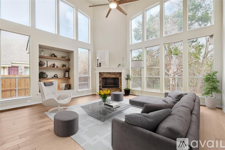 A living room with a grey sofa, a white chair, and a glass table with a vase of flowers on it.