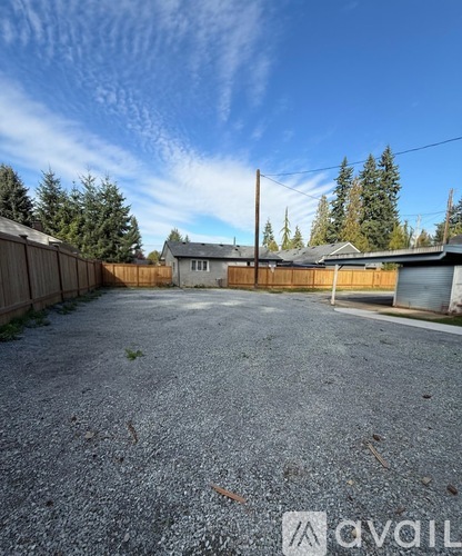A gravel driveway leads to a house with a wooden fence and trees in the background.