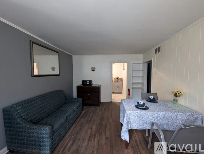 A living room with a grey couch, a small table with a vase of flowers, and a mirror on the wall.