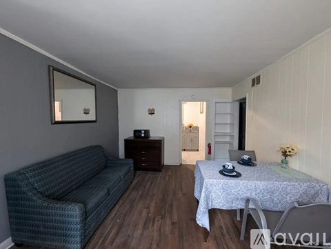 A living room with a grey couch, a small table with a vase of flowers, and a mirror on the wall.