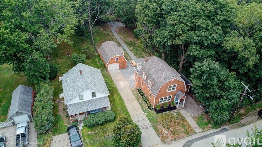 A house with a red brick exterior is surrounded by trees and has a driveway leading to the front door.