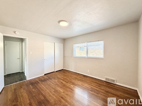 A room with wooden floors and a window showing a building outside.