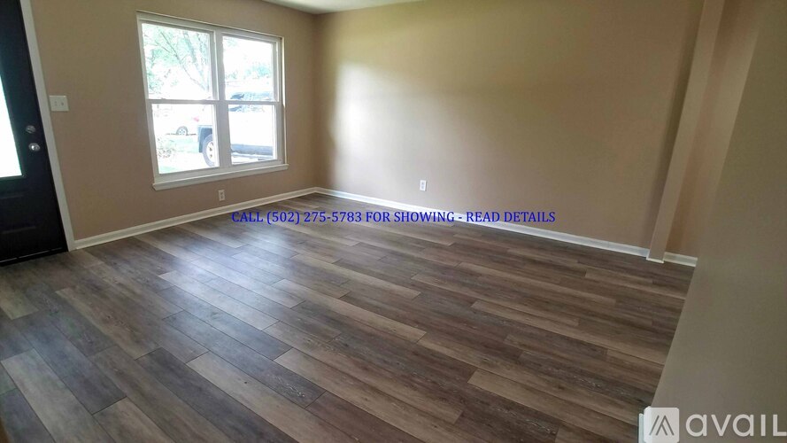 A room with wooden flooring and a window showing a parking lot outside.