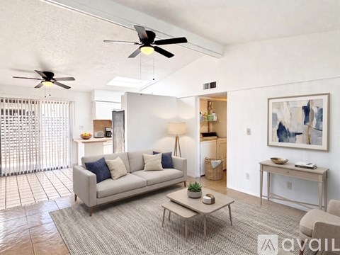 A living room with a grey couch, a coffee table, a ceiling fan, and a painting on the wall.