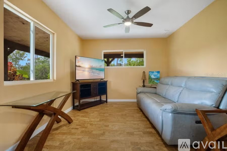 A living room with a grey couch, a glass table, and a ceiling fan.