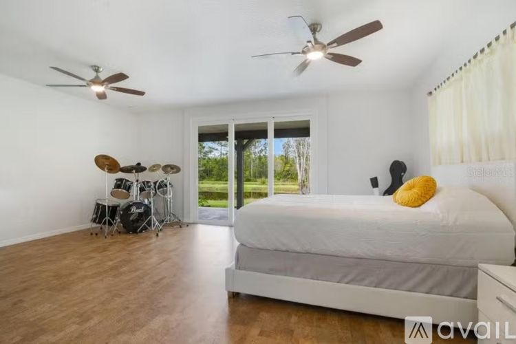 A bedroom with a bed, a drum set, and a ceiling fan.