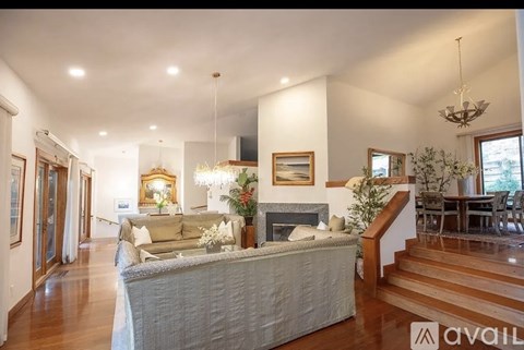A well-lit, spacious living room with a grey sofa and a chandelier.