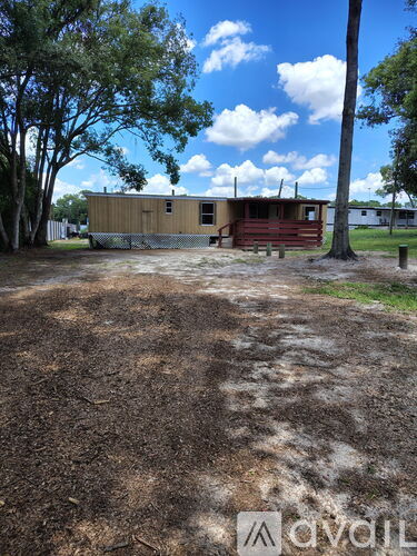 A brown wooden building with a red door is surrounded by a dirt field.