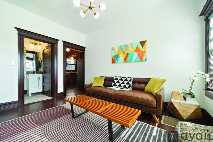 A living room with a brown couch and a colorful painting on the wall.