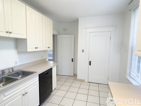 A kitchen with white cabinets and a black trash can.