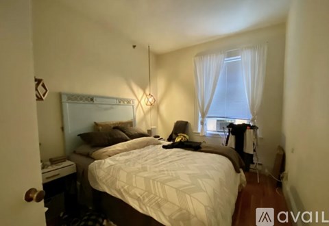 A bedroom with a large bed and a window with white curtains.