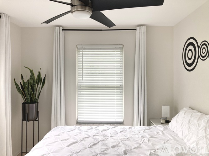 A bedroom with a bed, a ceiling fan, a potted plant, and a wall art.